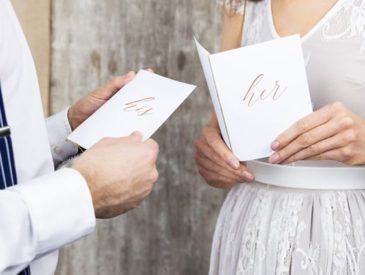 Bruid en bruidegom die gelofte boekjes vasthebben met 'His' en 'Her' op.